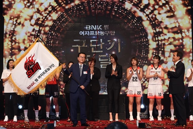 이두호 BNK캐피탈 대표이사(가운데)가 구단기를 흔들고 있다. /사진=WKBL 제공